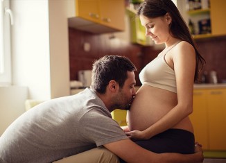 Mujer embarazada con su marido dándole un beso en la tripa