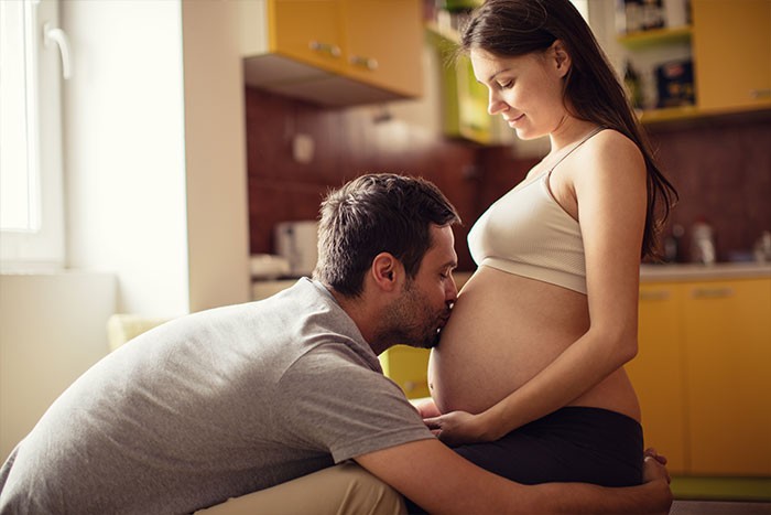 Mujer embarazada con su marido dándole un beso en la tripa