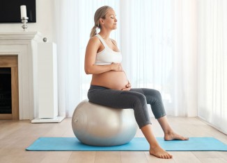 Mujer embarazada ejercitando su suelo pélvico con un fitball en el salón de su casa