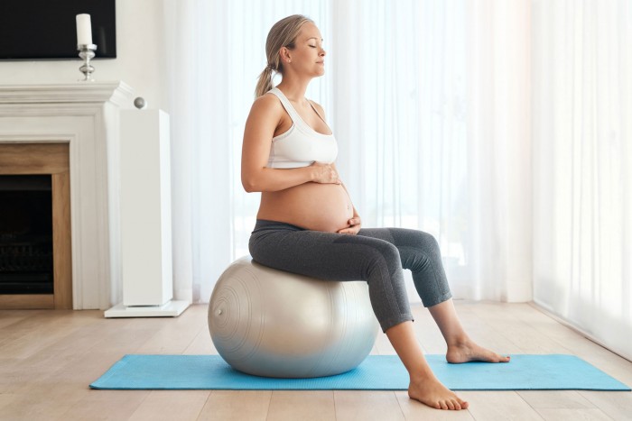 Mujer embarazada ejercitando su suelo pélvico con un fitball en el salón de su casa